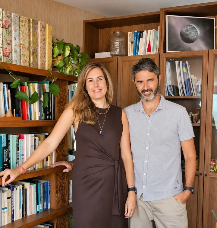 Ángela Gutiérrez y Jesús Martínez sonriendo juntos frente a una estantería de madera con libros, en su consulta